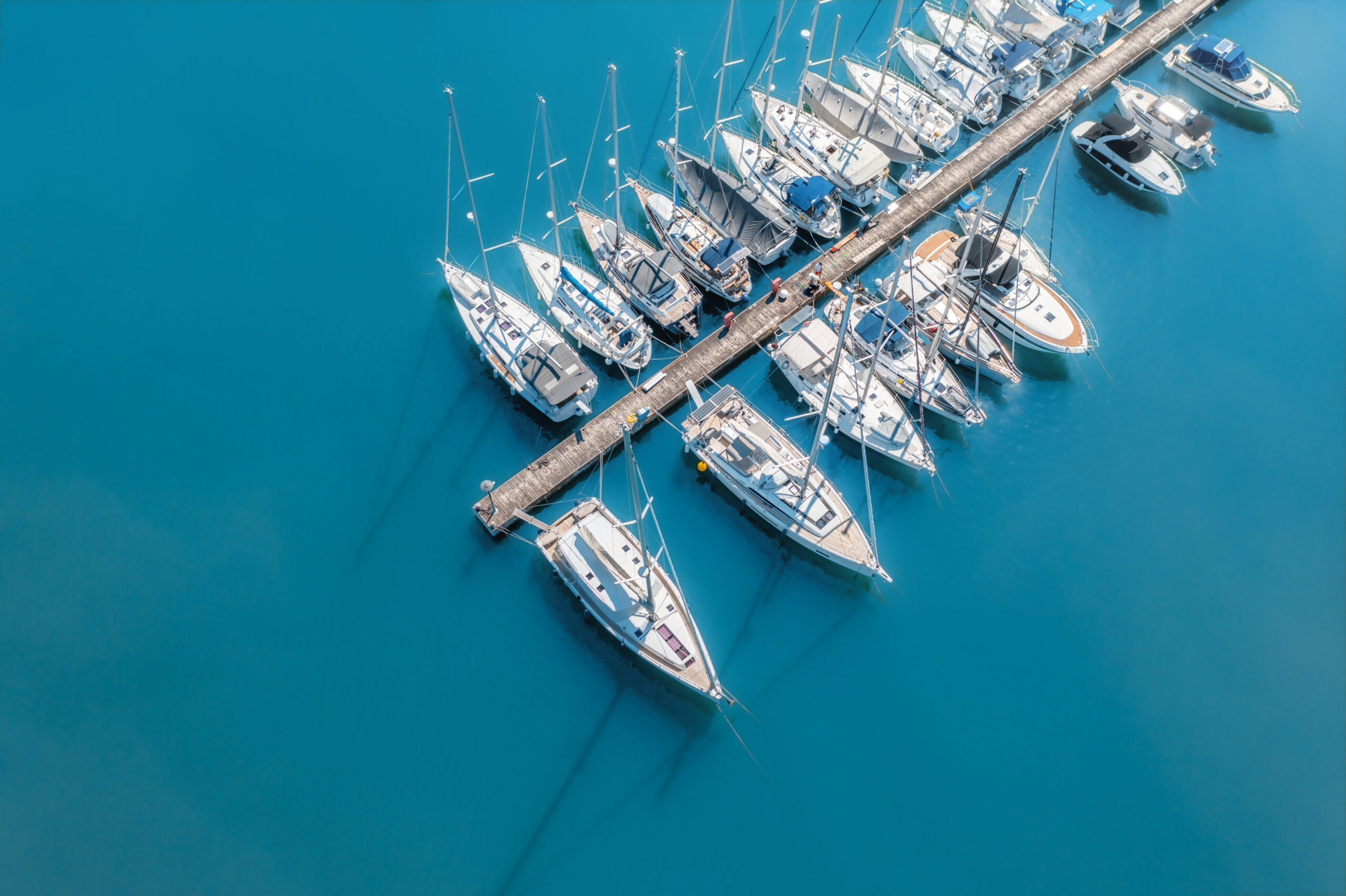 Aerial view of yachts and motorboats moored in a port with clear blue water in summer.
