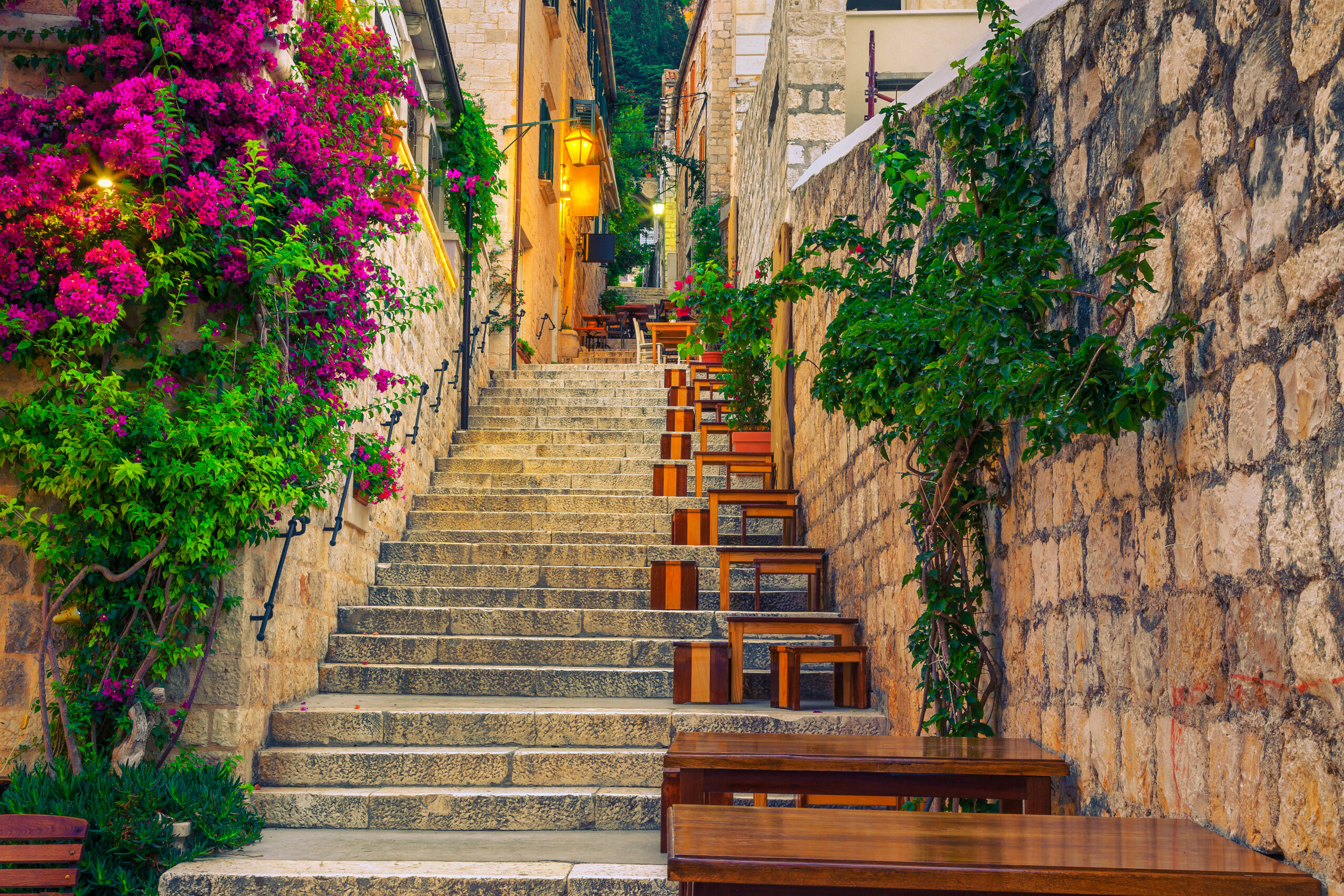 Cozy narrow street with street cafe and restaurant at morning. Rustic street with stone houses and colorful bougainvillea mediterranean flowers.