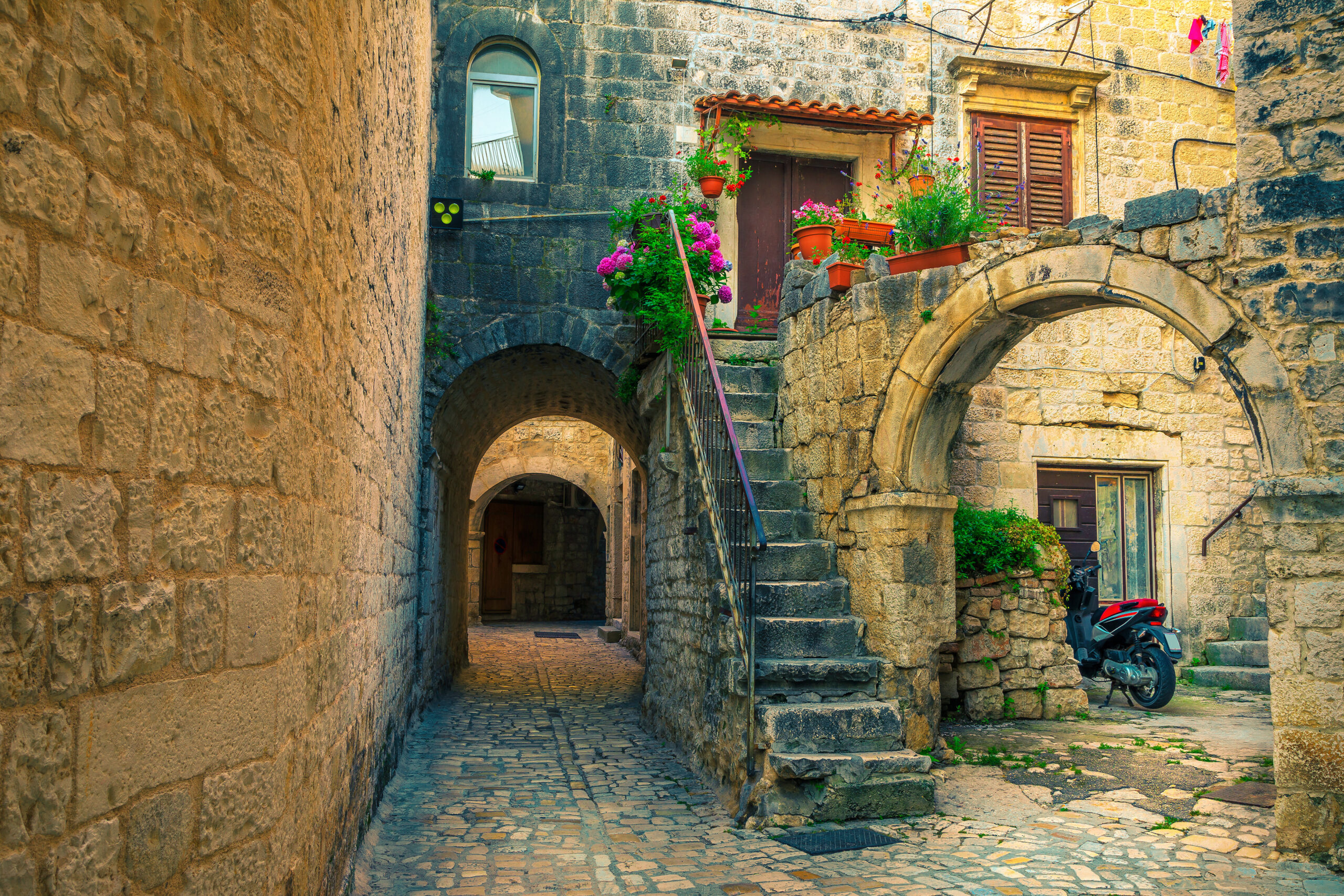 Picturesque narrow street with stone houses. Rustic stone houses and entrances decorated with flowers. Cozy street with antique houses and narrow alley.